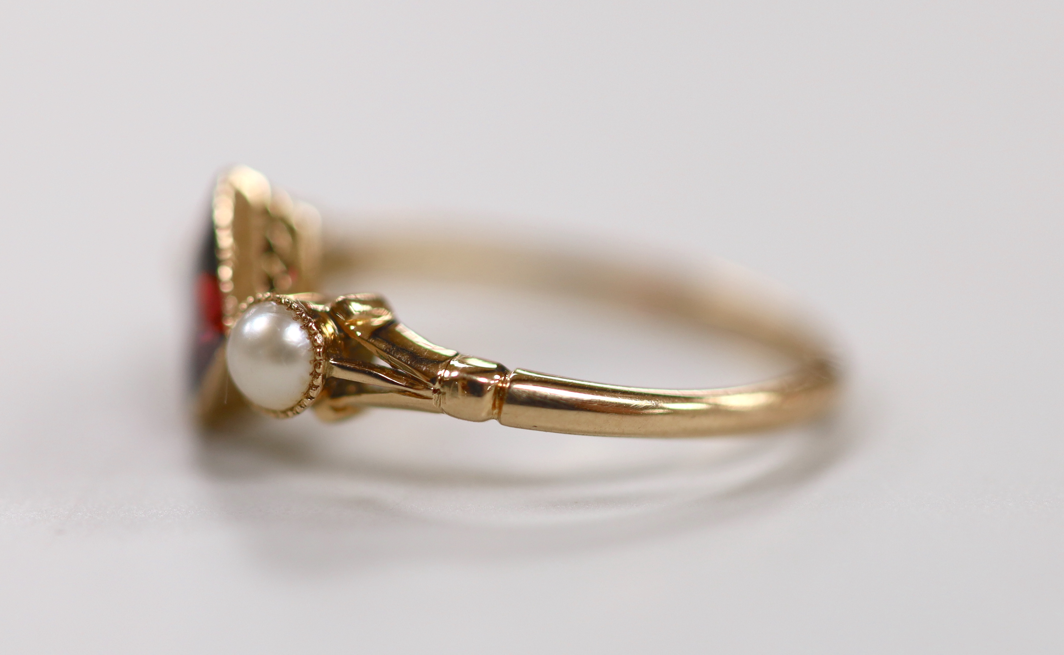 An early 20th century yellow metal, single stone garnet and two stone split pearl set ring, size N, gross weight 2.2 grams.